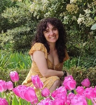 Fotografía de Isabel Pedrero, posando sobre un fondo vegetal y con rosas en la parte delantera; ella lleva un vestido veraniego de color amarillo